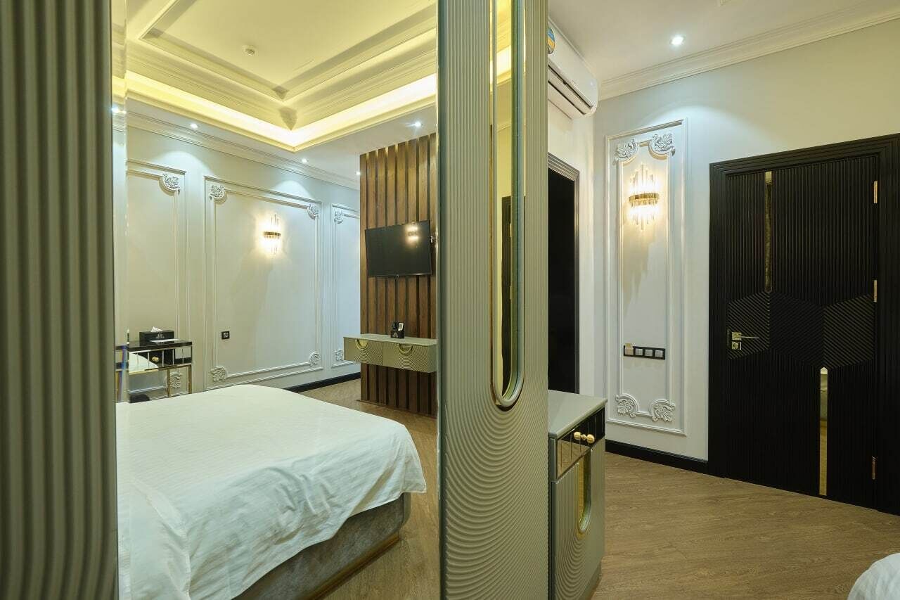 Habitación de hotel con cama, tocador con espejo, televisor y puerta con lámpara.