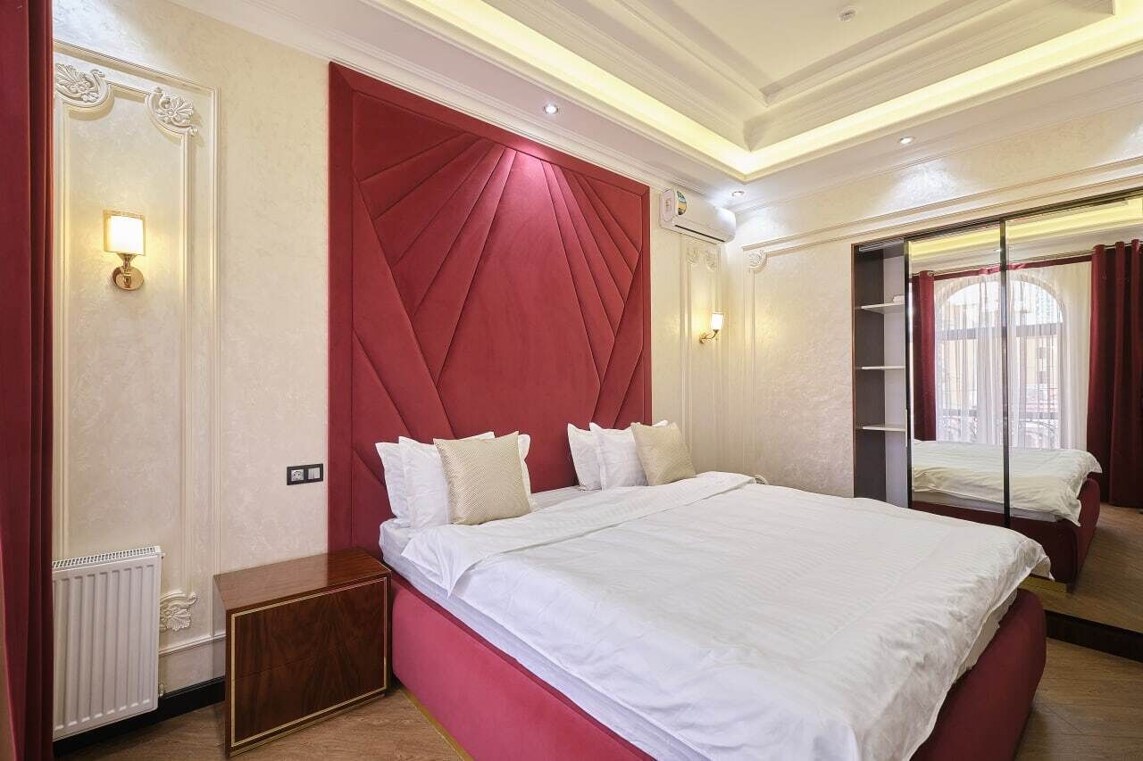 A hotel room with a large bed, a red accent wall, and a window with curtains.