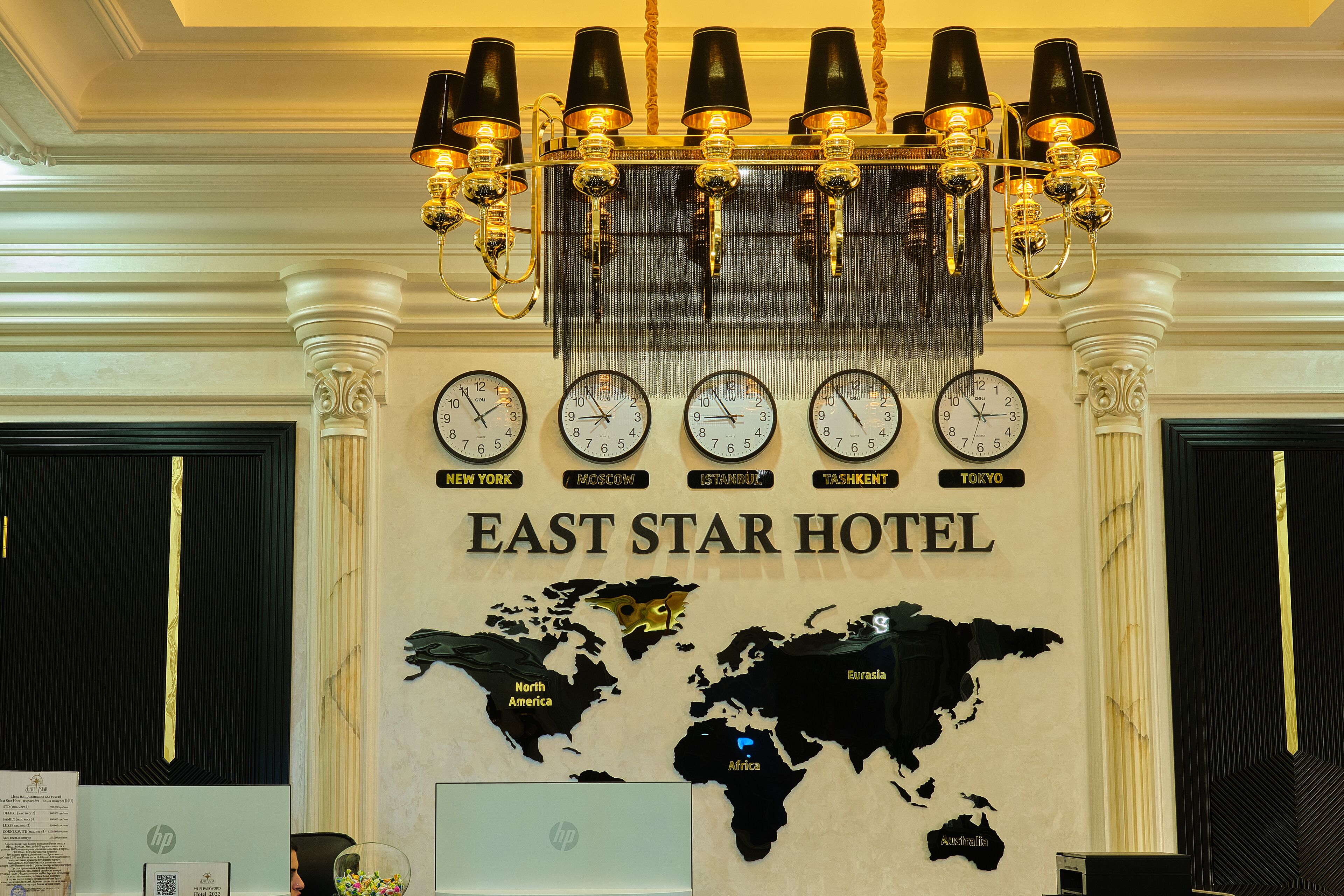 A hotel lobby with a world map, clocks displaying different cities, and a chandelier.