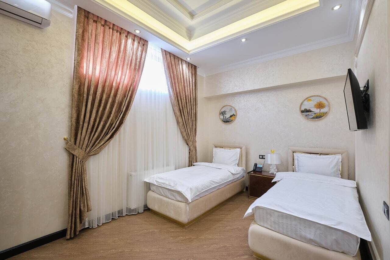 A hotel room with two beds, a flat-screen TV mounted on the wall, and a small bedside table with a lamp.