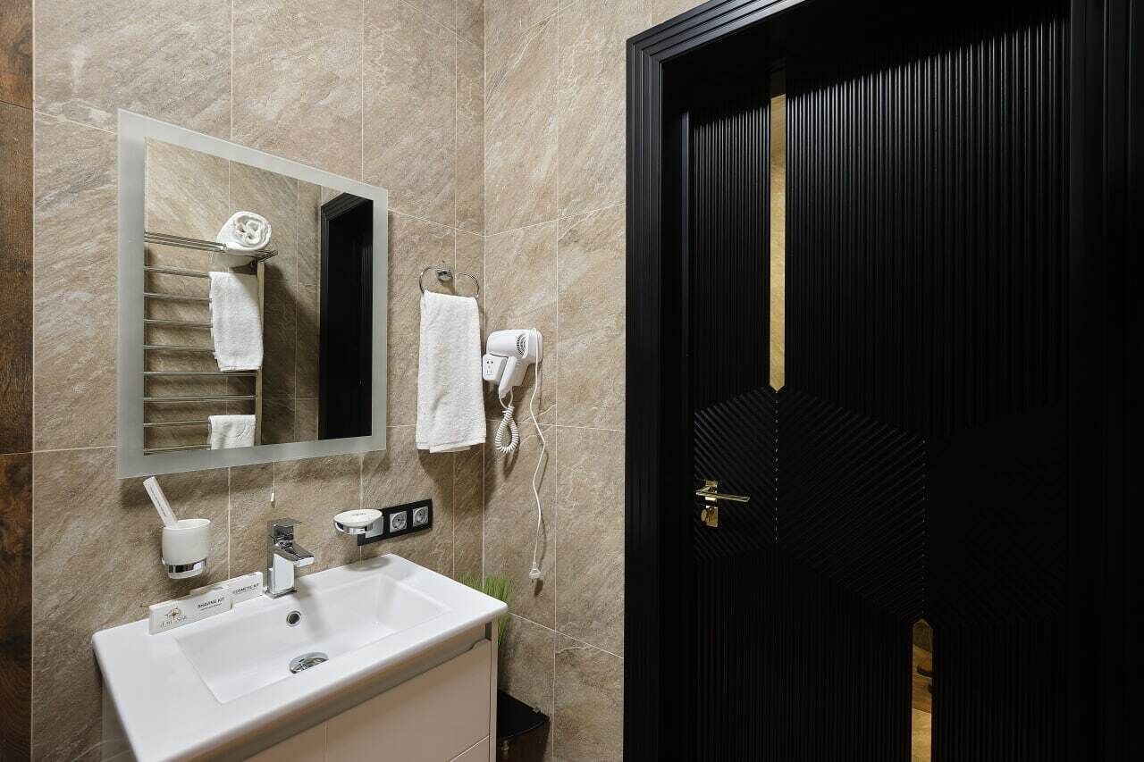 A bathroom with a white sink, a mirror, a towel rack, and a black door.