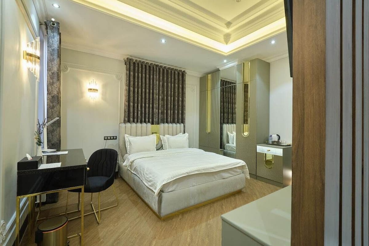A modern hotel room with a bed, desk, chair, and a small bathroom area.