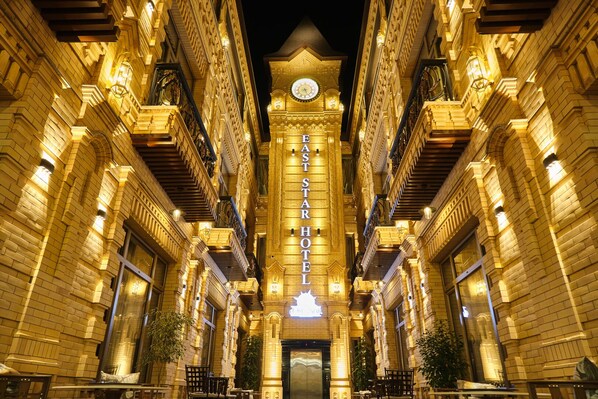 A grand hotel facade with a prominent clock tower, multiple balconies, and a central entrance. - East Star Hotel (Samarkand)