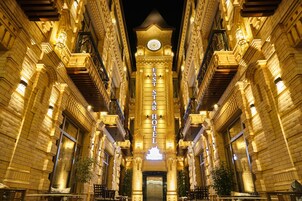 A grand hotel facade with a prominent clock tower, multiple balconies, and a central entrance.