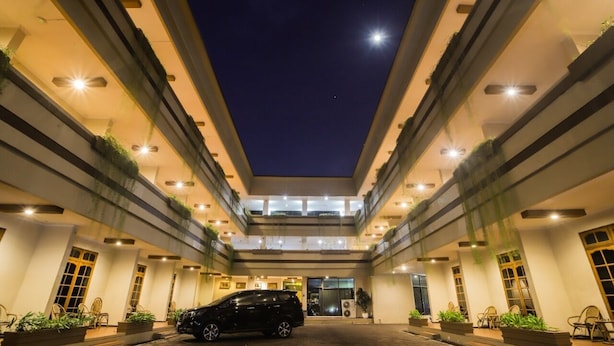 Een hotelgevel met een geparkeerde auto ervoor, meerdere verdiepingen en een nachtelijke hemel.