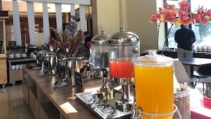 Een ontbijtbuffet met koffiezetapparaten, een fruitsapdispenser en een koffiepot.