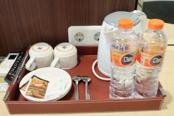 A hotel room's breakfast tray with a coffee maker, two mugs, a plate with a packet, two spoons, two bottles of water, and a remote control.