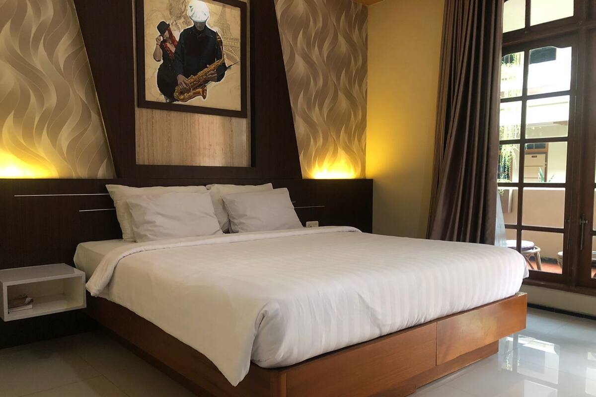 Een moderne slaapkamer met een groot bed, twee nachtkastjes, een kunstwerk aan de muur en uitzicht buiten door een raam.