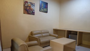 Een woonkamer met een beige bank, een salontafel en een flatscreen-televisie op een standaard. Twee decoraties hangen aan de muur, één met een muzieknoot en de andere met de tekst 'Celebrate Jazz'.