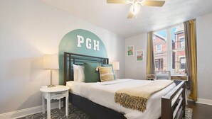 Una camera d'albergo con un letto, un comodino, una ventola a soffitto e una finestra con tende.