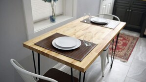 Un tavolo da pranzo con piano in legno e gambe in metallo, apparecchiato con piatti bianchi e un bicchiere.