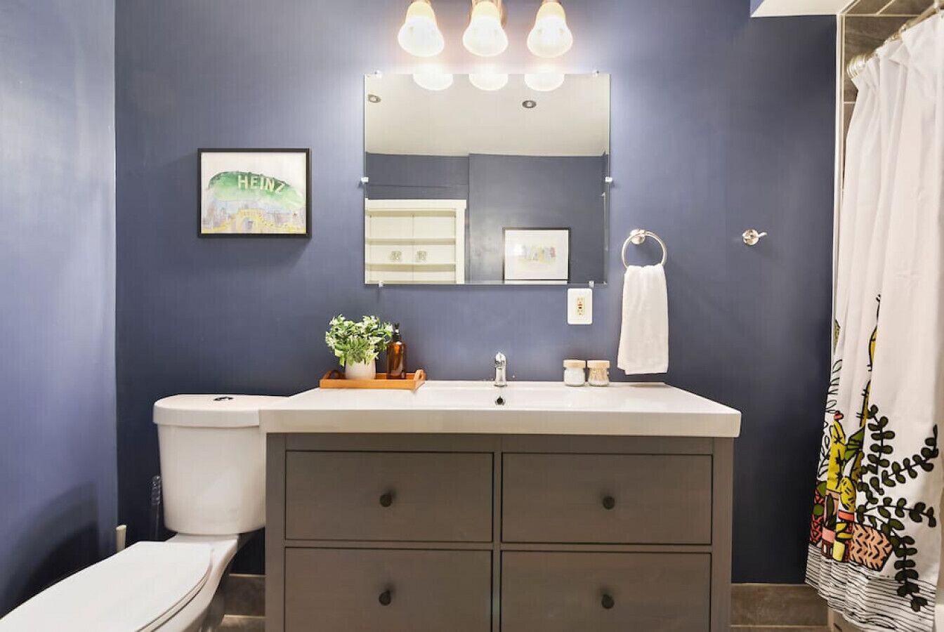 A bathroom with a dark blue wall, a white sink with a mirror above it, and a shower curtain with a leaf pattern.