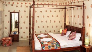 A four-poster bed with a colorful quilt, a wooden floor, and patterned wallpaper. - Desert Safari Camping Jaisalmer  (Jaisalmer)