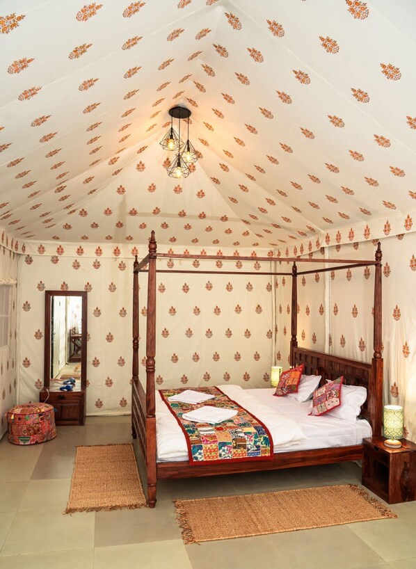 A four-poster bed with a colorful quilt, a wooden floor, and patterned wallpaper.