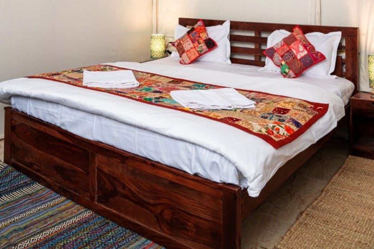Un letto rifatto con cura, con una coperta a fantasia, una testiera in legno e una lampada a sospensione.