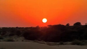 A sunset over a desert landscape with sparse vegetation and a clear sky. - Desert Safari Camping Jaisalmer  (Jaisalmer)