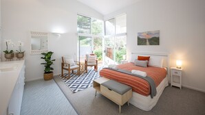 Ein Schlafzimmer mit großem Fenster, einem Bett, einem Nachttisch, einem Sessel, einem kleinen Tisch und einem Blumentopf.