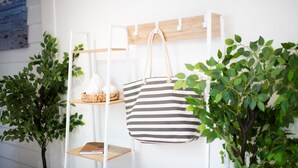 Eine geteilte Tragetasche hängt an einem weißen Metallgestell mit Regalen darunter, umgeben von Grünpflanzen.