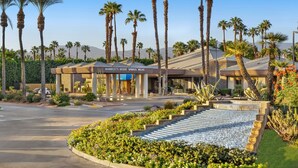 Un hotel con entrada temática de desierto, palmeras y un área ajardinada con escalones que llevan a una piscina.