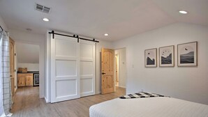 Ein Schlafzimmer mit einem Bett, einer Schiebetür, einer Holztür und einem durch eine offene Tür einsehbarer Küchenbereich.