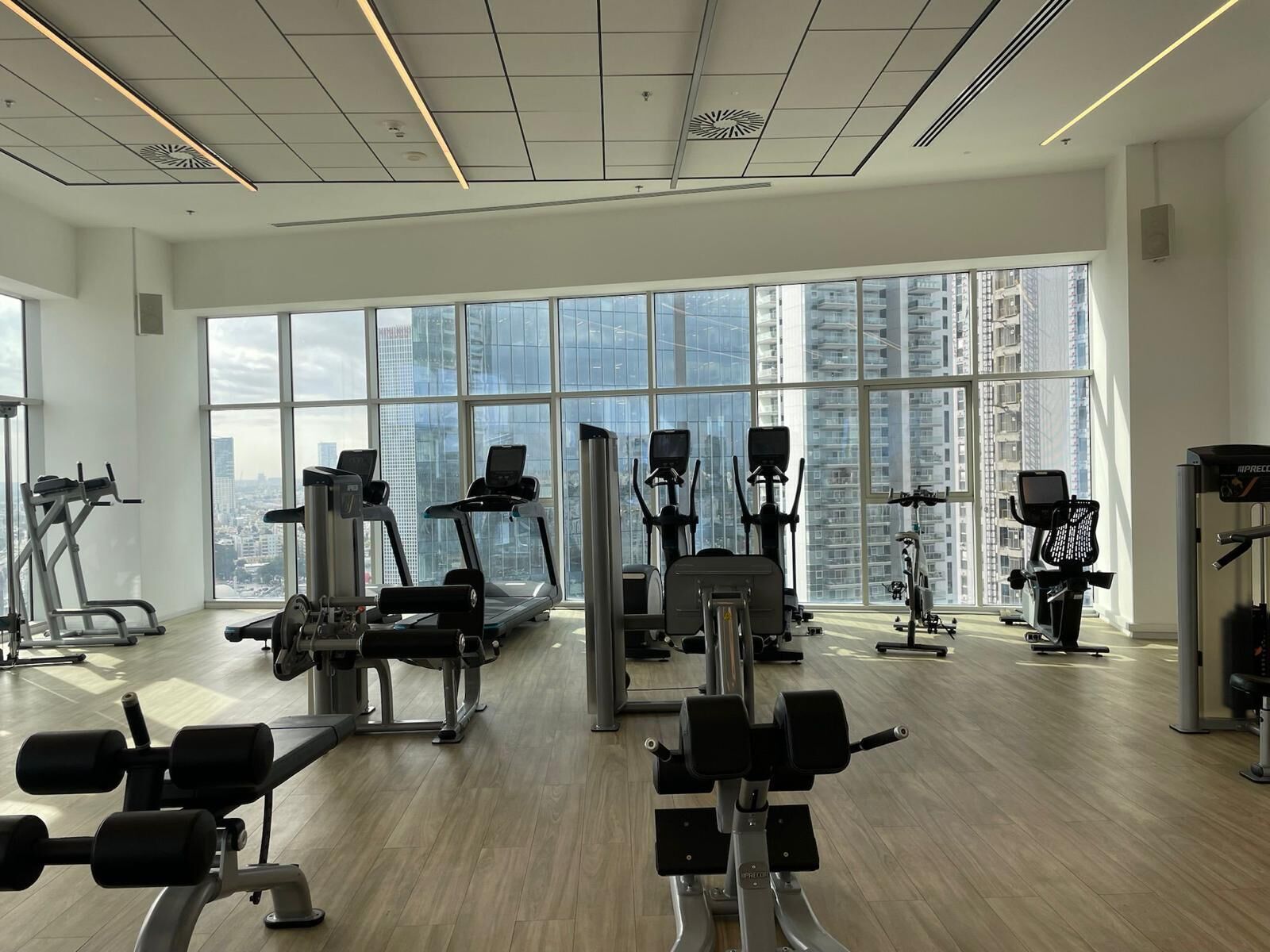 Een moderne sportschool met diverse fitnessapparaten, grote ramen met uitzicht op de stad en een schoon, ruim interieur.