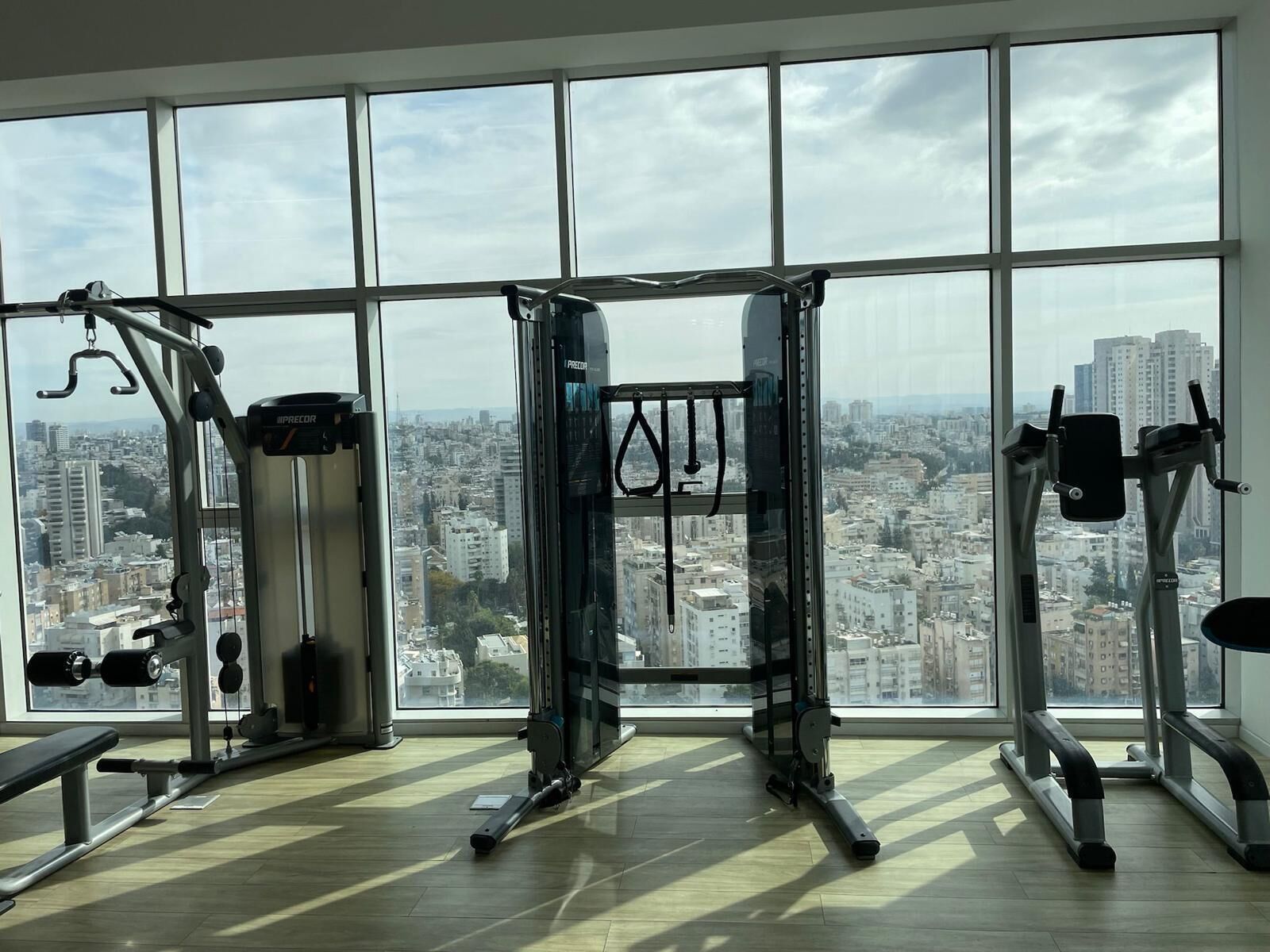 A gym with large windows, various exercise equipment, and a city view.