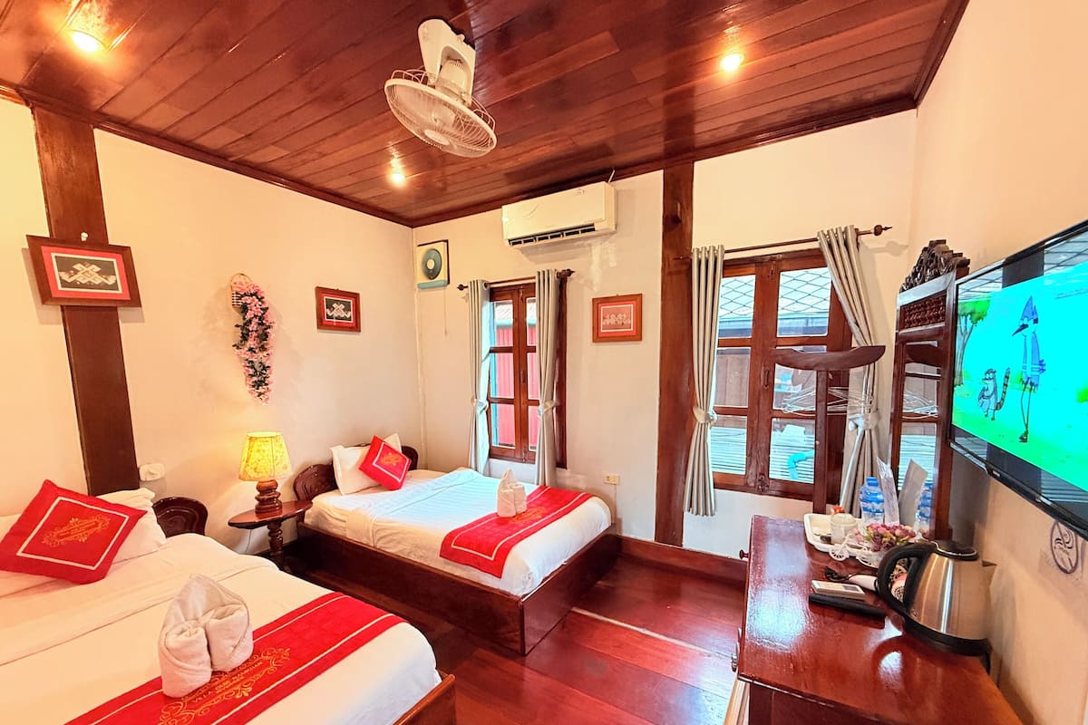 A hotel room with two beds, a wooden ceiling, a TV, and a desk with a kettle.