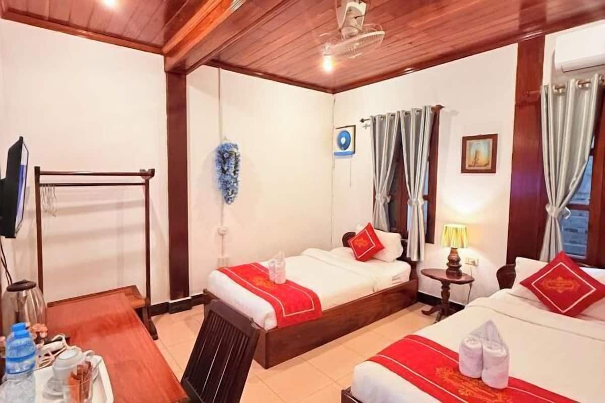 A hotel room with two beds, a wooden ceiling, a small table, and a TV.