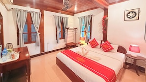 Une chambre d’hôtel équipée d’un lit, d’un bureau, d’une chaise, d’une petite table et d’un ventilateur fixé au mur.