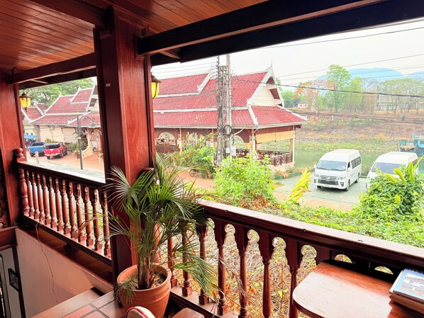 A wooden balcony with a potted plant, a view of a red-roofed building, and a parked white van.