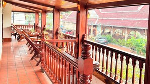 Un couloir en bois, doté d’un sol carrelé, d’une rambarde et offrant une vue sur un bâtiment traditionnel à toit rouge.