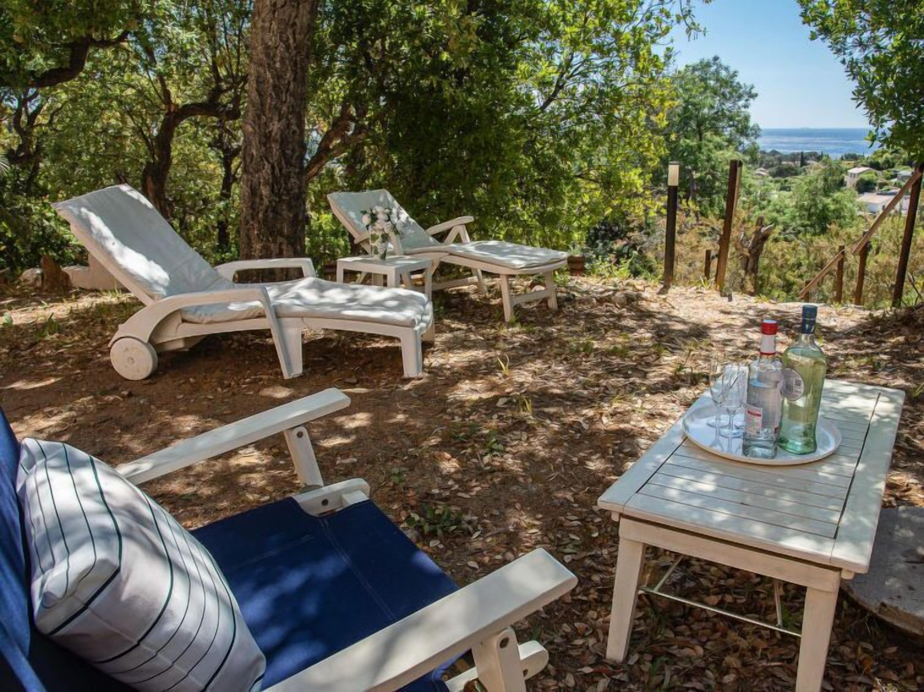 A patio with lounge chairs and a table with drinks, surrounded by trees and a view of the landscape.