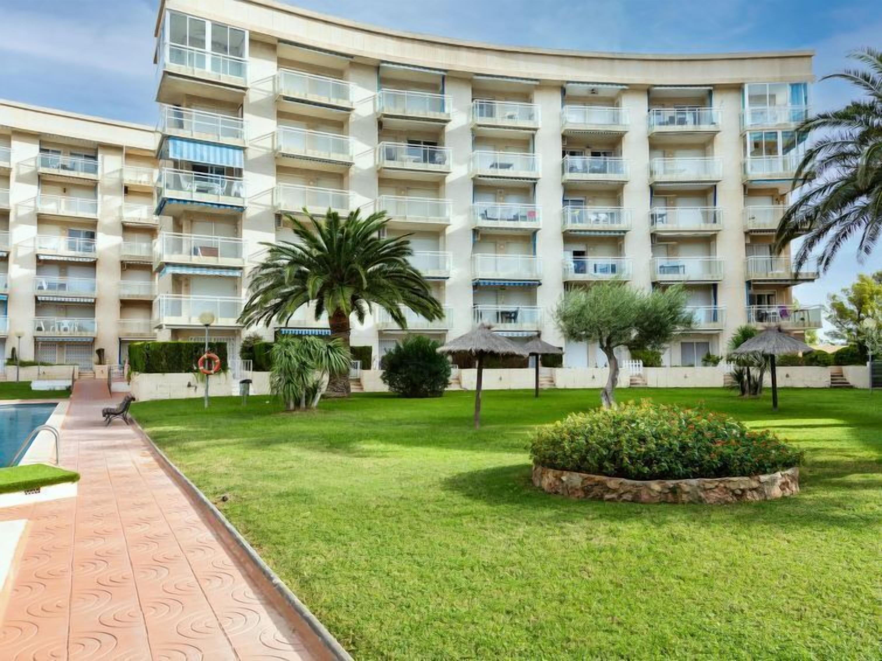 Un hotel de varios pisos con balcones, piscina y jardines cuidados.