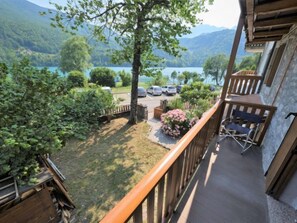 Un balcon avec vue sur un lac et des montagnes, une terrasse en bois et un espace salon extérieur.