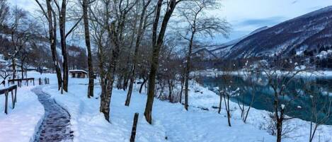 A snow-covered path leading to a cabin by a lake with mountains in the background.