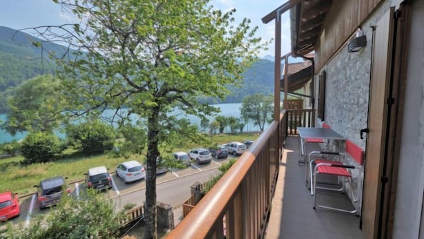A balcony with a view of a lake and mountains, a table with chairs, and parked cars. - Apartment Elsa by Interhome (Barcis Lake)
