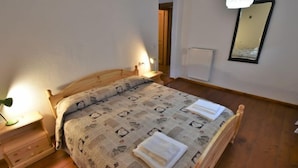 A wooden bed with a patterned bedspread and two pillows, a bedside lamp, a nightstand, a mirror, and a radiator on the wall. - Apartment Elsa by Interhome (Barcis Lake)