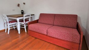 A room with a red sofa, white chairs, and a wooden table. - Apartment Elsa by Interhome (Barcis Lake)
