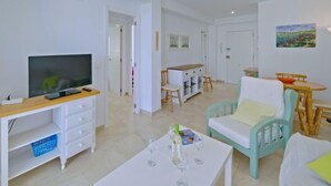 A modern living room with a TV, white furniture, a dining area, and a painting on the wall. - La Luz 12 by Interhome (Calpe/Calp)