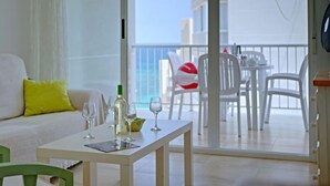 A balcony with a table set for dining, a sofa with a yellow pillow, and a view of the sea. - La Luz 12 by Interhome (Calpe/Calp)