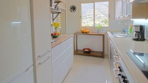 Una cocina compacta con refrigerador, pileta, ventana con vista y una mesita con frutas.