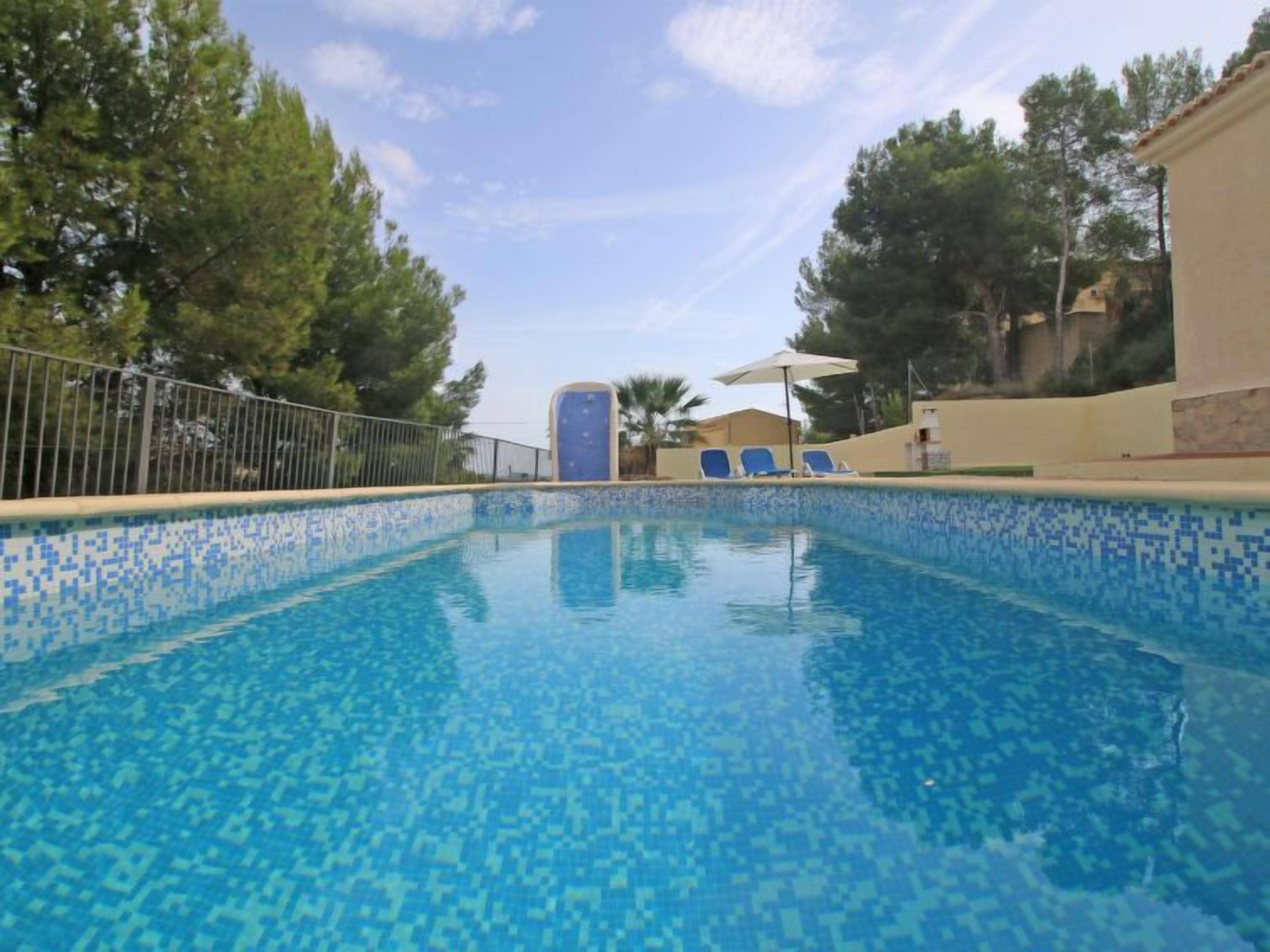 A swimming pool with blue mosaic tiles, surrounded by trees and a fence.