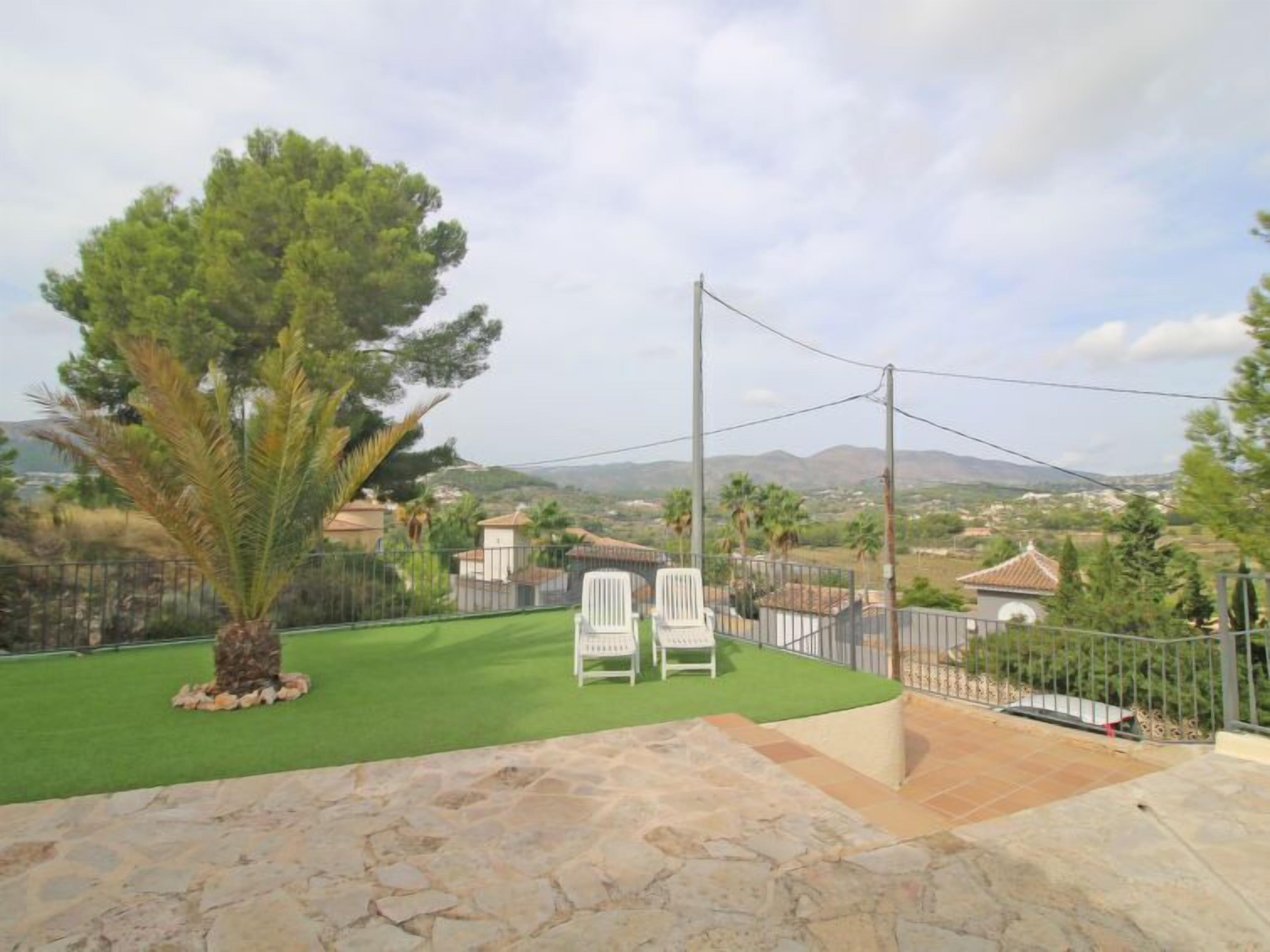 A patio area with stone flooring, two white chairs, and a green lawn.