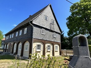 Una casa de dos pisos con un tejado empinado, varias ventanas y una chimenea de piedra.