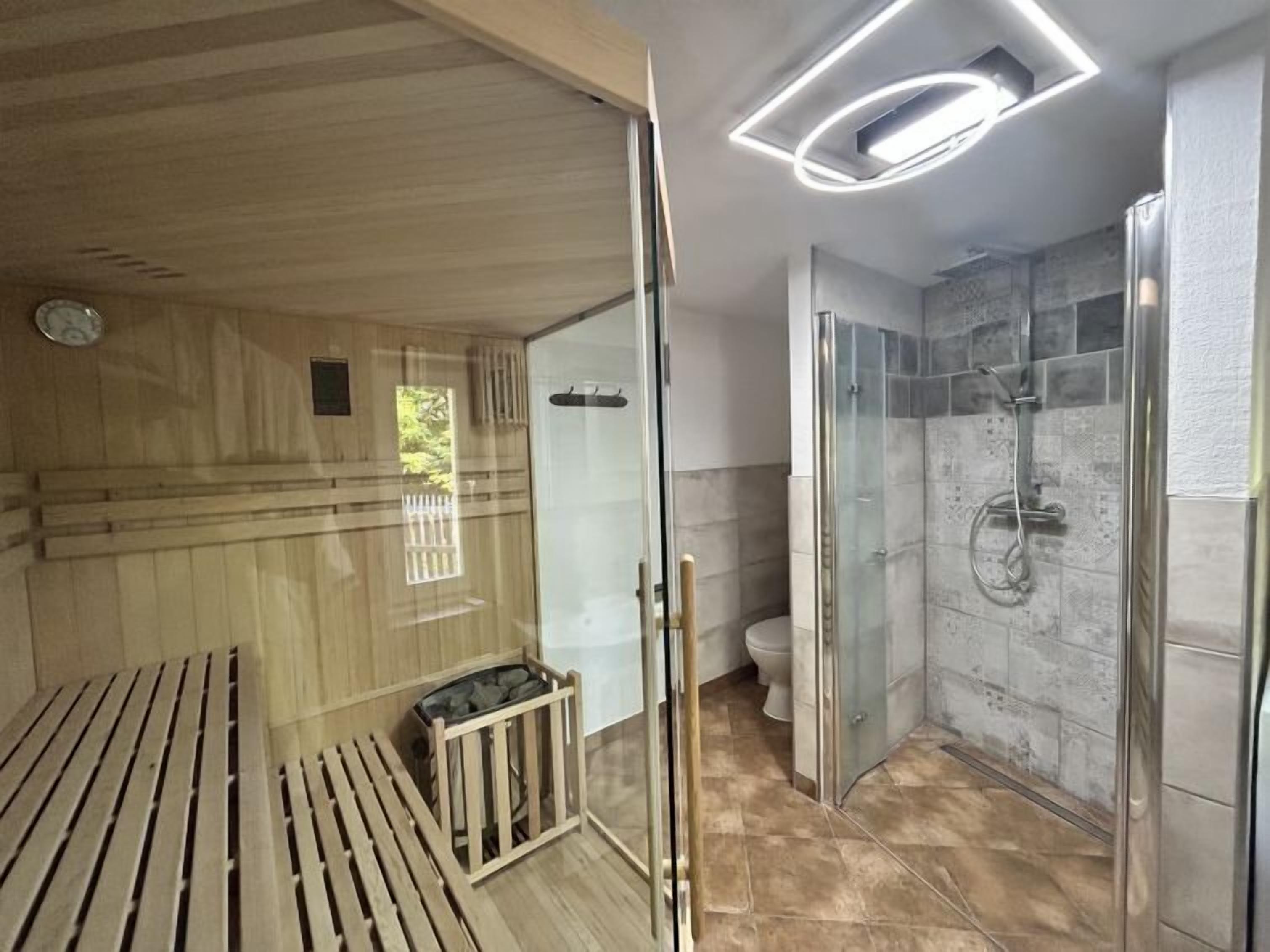 Une salle de bain moderne avec une douche à parois de verre, un banc en bois et des toilettes apparentes.