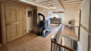 A spacious room with a wooden floor, a fireplace, a sofa, and a staircase. - Apartment Frushi by Interhome (Grossschönau)