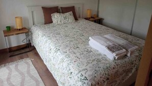Une chambre  à coucher avec un lit, deux tables de chevet, une commode, une couvre-lit à motifs et une serviette pliée posée sur le lit.