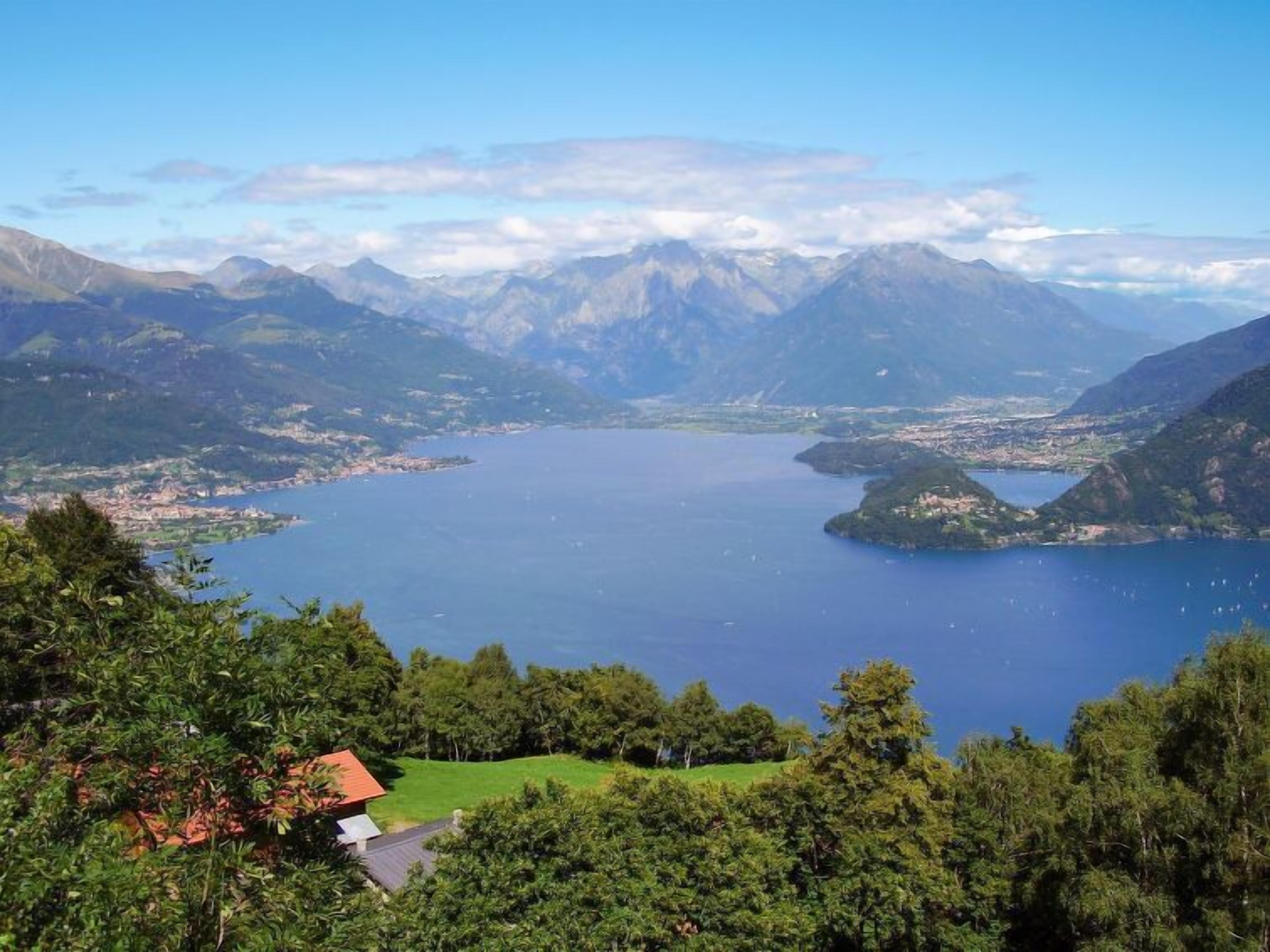 Un paisaje montañoso con un lago, un pequeño edificio de techo rojo y abundante vegetación.