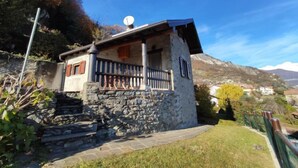 Et stenhus med balkon, parabolantenne og et bjerglandskab i baggrunden.