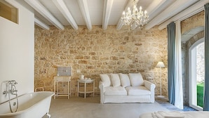 A bathroom with a stone wall, a bathtub, a white sofa, and a chandelier.